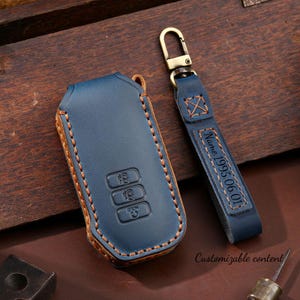 May include: A blue leather key fob case and matching strap with a metal clasp. The case has three buttons and contrasting tan stitching. The strap is engraved with "Name 1995.06.01" and the words "Customizable content".