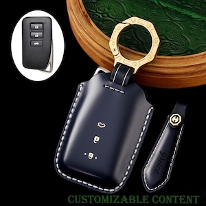 Puede incluir: Un estuche para llavero de cuero azul marino con costuras blancas y un llavero dorado. La funda tiene símbolos en relieve y una etiqueta a juego con la palabra "grace". Una llave de coche se muestra en la esquina superior izquierda. El texto "CUSTOMIZABLE CONTENT" está en la parte inferior.