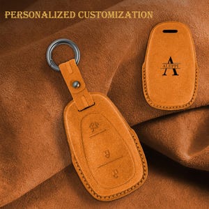 Può includere: Custodia per portachiavi in pelle arancione con anello in metallo e la scritta "ALEPPI". La custodia ha una chiusura a bottone ed è progettata per proteggere le chiavi dell'auto. L'immagine include anche il testo "PERSONALIZZAZIONE PERSONALIZZATA".