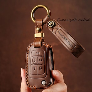 Peut inclure: Un porte-clés en cuir marron avec un anneau et des accessoires dorés. Le porte-clés présente un design cousu et comprend le texte "Customizable content" et "David 1995.06.01". Le porte-clés est conçu pour contenir une clé de voiture.