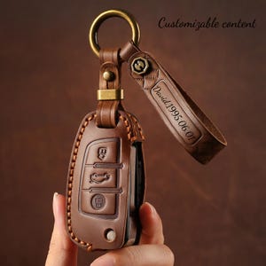 May include: Brown leather car key fob cover with a metal ring and strap. The key fob cover has embossed buttons and stitching. The strap is engraved with "David 1995.06.01". The text "Customizable content" is also visible.