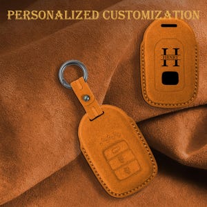 May include: Orange leather key fob cover with a silver keyring and the text "PERSONALIZED CUSTOMIZATION" in gold. The cover has embossed buttons and the initials "H HRNRY" in black.