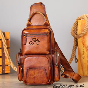 May include: A brown leather sling bag with multiple zippered compartments and a top handle. The bag features the word "Mr" in script on the front and "customized text" at the bottom. The bag has a shoulder strap and is designed to be worn across the body.