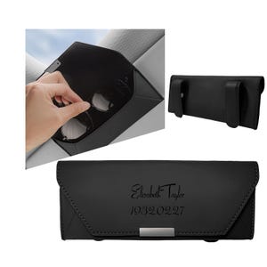 Puede incluir: Un estuche rectangular negro para gafas con cierre magnético y dos clips en la parte posterior. El frente está grabado con el texto Elizabeth Taylor y 19320227. El estuche presenta un acabado liso y un detalle metálico plateado en la base.