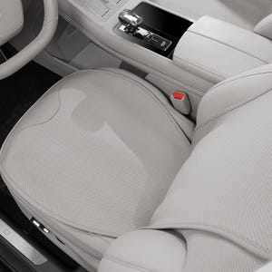 May include: A close-up of a light gray car interior, showcasing a perforated leather seat, armrest, and steering wheel. The image highlights the car's modern design with a focus on the seat's texture and the sleek dashboard.