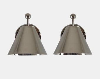 May include: A pair of wall-mounted sconces featuring a polished silver-tone metal finish. Each fixture consists of a conical shade attached to a circular backplate by a short, straight arm topped with a small spherical finial detail.