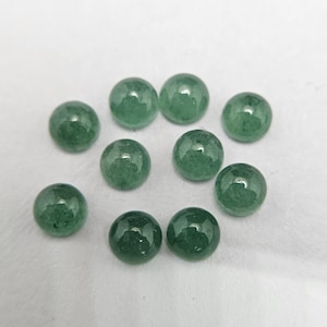 May include: A collection of ten polished, round, green gemstones. The stones are a vibrant shade of green, with a smooth, reflective surface. They are scattered on a white surface, showcasing their color and shape.