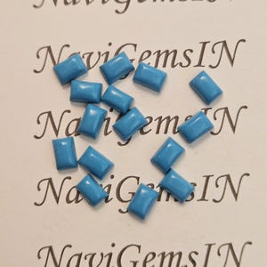 Puede incluir: Un conjunto de gemas rectangulares de color turquesa. Las gemas están distribuidas uniformemente sobre una superficie blanca con el texto "NaviGemsIN" en cursiva. Las gemas son de un tono azul vibrante.