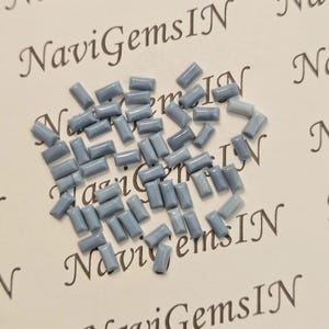 Peut inclure: Un ensemble de petits gemmes rectangulaires bleu clair dispersés sur une surface crème. Les gemmes sont de forme et de taille uniformes, avec un aspect poli. Le texte "NaviGemsIN" est imprimé en cursive.