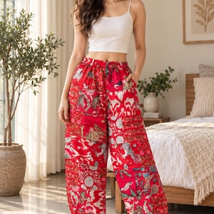 Könnte beinhalten: Ein weißes geripptes Tanktop kombiniert mit einer locker sitzenden roten Hose mit einem lebendigen Patchwork-Muster aus Blumen- und Vogelmotiven. Die Hose hat einen elastischen Bund und geraffte Beinabschlüsse, getragen mit weißen flauschigen Hausschuhen.