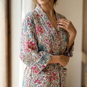 May include: A floral print robe with a white background, featuring pink, green, and blue botanical patterns. The robe has a white trim and a relaxed fit. This garment is suitable for lounging or as a light layer.