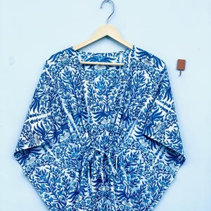 May include: A blue and white patterned kimono-style robe with a tie waist, hanging on a wooden hanger. The robe features a floral design in shades of blue against a white background. The sleeves are wide and the fabric appears lightweight.