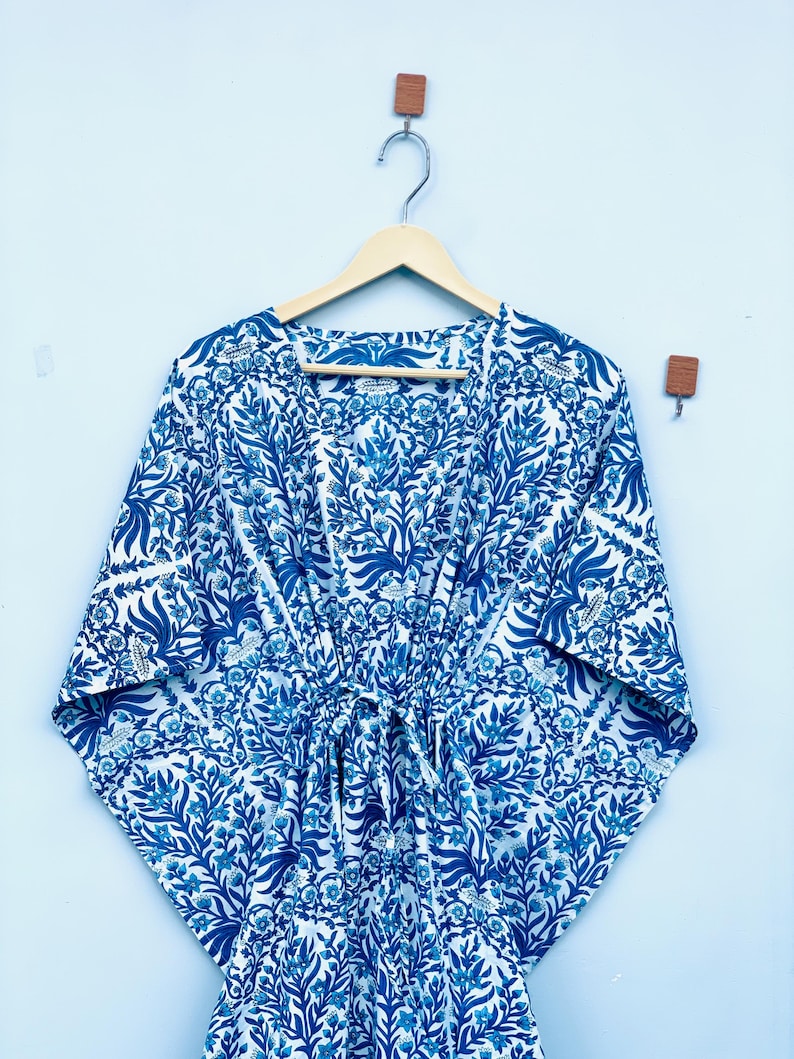 May include: A blue and white patterned kimono-style robe with a tie waist, hanging on a wooden hanger. The robe features a floral design in shades of blue against a white background. The sleeves are wide and the fabric appears lightweight.