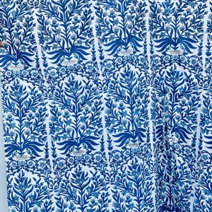 May include: White fabric with a repeating pattern of blue floral and leaf designs. The pattern features stylized trees and floral elements in varying shades of blue, creating a visually rich and detailed textile.