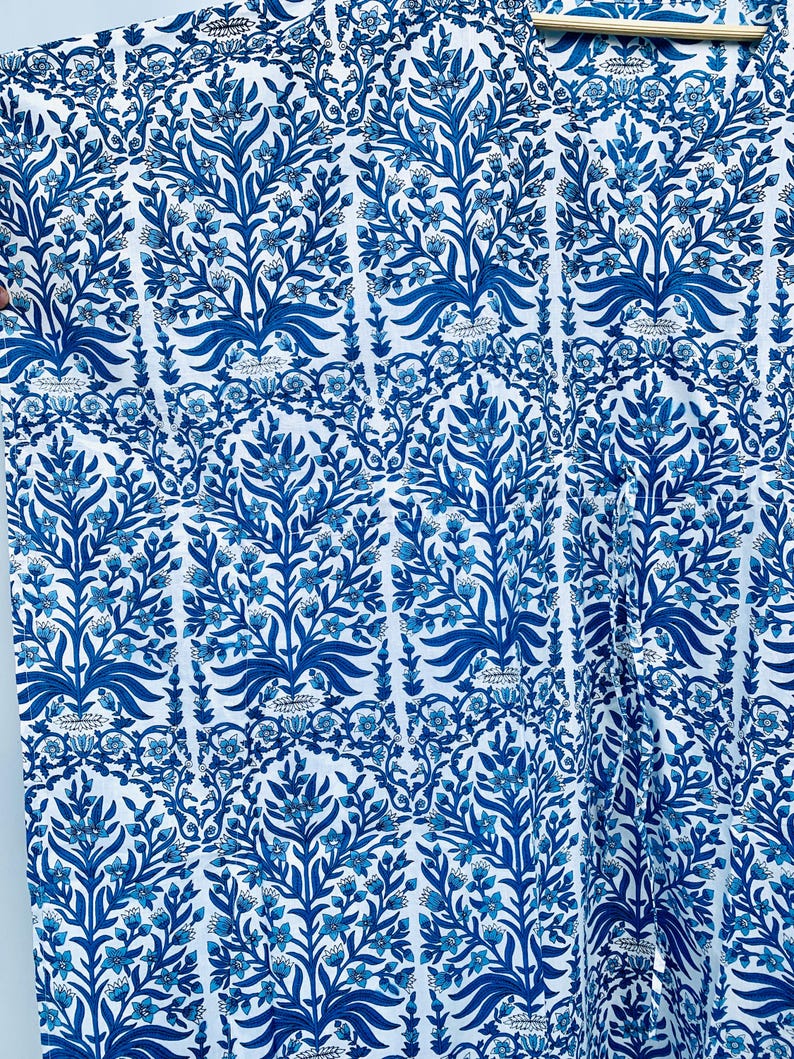 May include: White fabric with a repeating pattern of blue floral and leaf designs. The pattern features stylized trees and floral elements in varying shades of blue, creating a visually rich and detailed textile.
