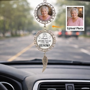 May include: Silver car charm with a photo of a woman in a pink shirt. The charm has a decorative frame and the text "I have an angel watching over me I call her GRANDMA." A small wing charm hangs below.