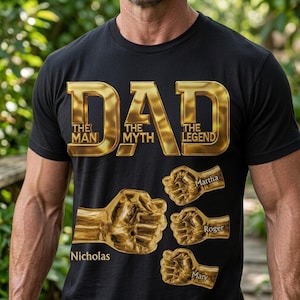 May include: A black t-shirt featuring large gold metallic text that reads DAD THE MAN THE MYTH THE LEGEND. Below the text are four gold metallic fist graphics of varying sizes, each labeled with the names Nicholas, Martha, Roger, and Mary.