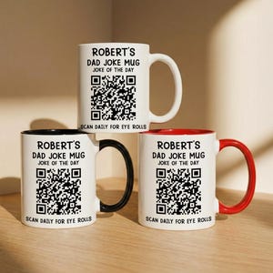 May include: Three white ceramic mugs featuring black text that reads Robert's Dad Joke Mug, Joke of the Day, and Scan Daily for Eye Rolls, along with a QR code. One mug has a white handle, one has a black handle, and one has a red handle.