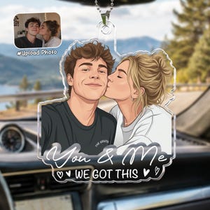 May include: A clear acrylic car ornament featuring a custom cartoon-style illustration of a couple, with the woman kissing the man on the cheek. The text "You & Me" and "WE GOT THIS" is printed in white script and block lettering below the couple.