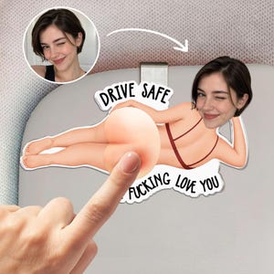 Peut inclure: Un clip de pare-soleil de voiture personnalisé avec une illustration de dessin animé d'une personne allongée en bikini rouge avec une photo de visage. Le texte indique DRIVE SAFE et I FUCKING LOVE YOU. Le design est imprimé sur une forme en acrylique.