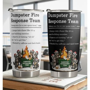 May include: Two stainless steel travel mugs with black lids. One is white, the other black. Both feature the text "Dumpster Fire Response Team" with a definition and raccoon graphic. The definition includes three points about teamwork and humour.