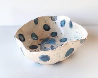 May include: A handmade ceramic bowl with a cream-colored base and dark blue polka dots. The bowl has an irregular, wavy rim and a blue fish design in the center. The bowl is suitable for serving or display.