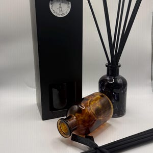 May include: A black rectangular gift box with a bow and a circular label reading Musk & Tonka, a dark glass diffuser bottle with black reeds, and a second amber-coloured glass bottle with a tortoiseshell pattern lying on its side.