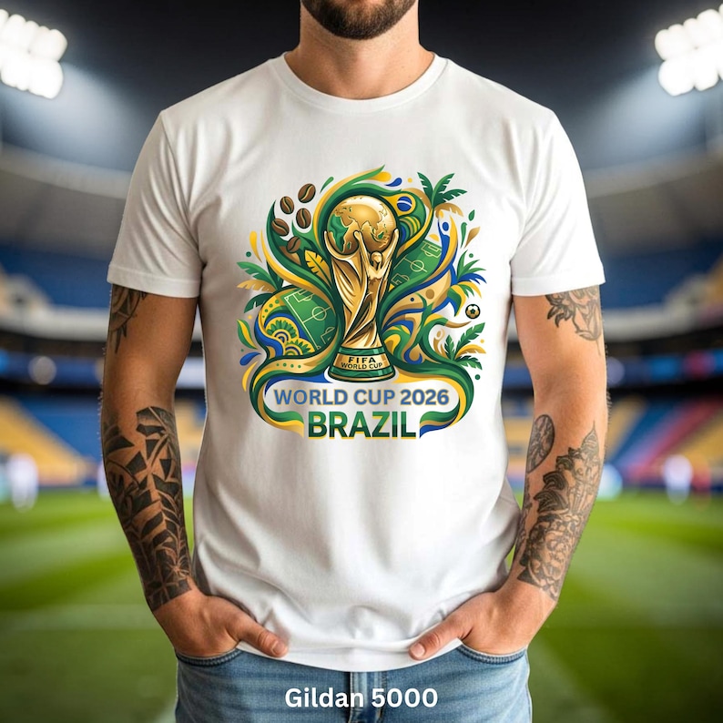 May include: White t-shirt with a vibrant graphic of the FIFA World Cup trophy, the text "WORLD CUP 2026 BRAZIL", and coffee beans. The design incorporates green, yellow, and blue. The shirt is a Gildan 5000.