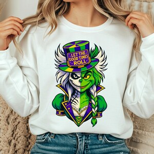 Könnte beinhalten: Weißes Sweatshirt mit einer Grafik einer grün-weißen Figur mit Zylinder. Der Hut trägt den Text "LET THE GOOD TIMES ROLL". Die Figur hat auf der einen Seite ein grünes Gesicht und auf der anderen einen weißen Totenkopf.
