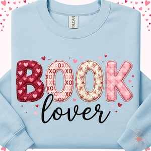 Może przedstawiać: Jasnoniebieska bluza z napisem "BOOK lover". Litery ozdobione są sercami i kwiatowymi wzorami. "B" i "K" są różowe, "O" są kwiatowe, a "B" ma wzór serca. Małe serca i akcenty "XO XO" są rozrzucone.