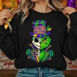Könnte beinhalten: Schwarzes Sweatshirt mit einer Grafik eines grünen und skelettartigen Charakters, der einen lila und grünen Zylinder und eine Jacke trägt. Der Text "LET THE GOOD TIMES + ROLL+" befindet sich auf dem Hut.