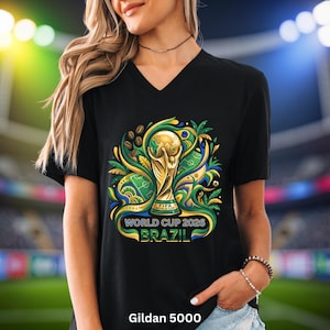 May include: Black V-neck t-shirt with a vibrant graphic of the FIFA World Cup trophy, football pitch, and coffee beans. Text reads "WORLD CUP 2026 BRAZIL". The shirt is a Gildan 5000.