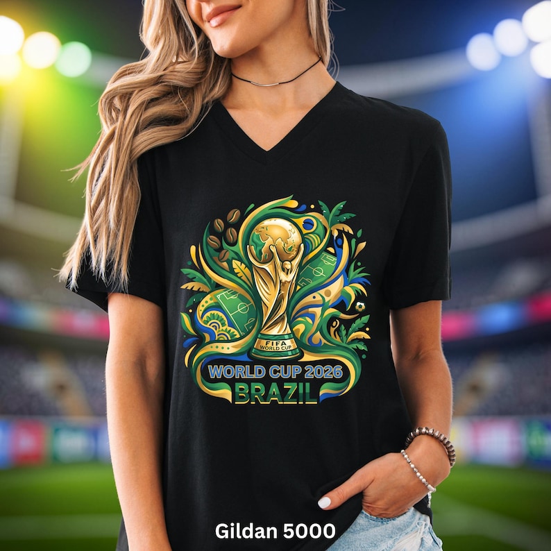 May include: Black V-neck t-shirt with a vibrant graphic of the FIFA World Cup trophy, football pitch, and coffee beans. Text reads "WORLD CUP 2026 BRAZIL". The shirt is a Gildan 5000.