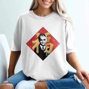May include: White t-shirt with a graphic of a person in a suit inside a red diamond. The diamond has gold Chinese characters. The person in the graphic is wearing a black suit and tie. The t-shirt is a casual style.