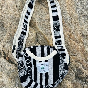 May include: A black and white striped crossbody bag with a matching strap. The bag has a circular design with a white trim and a label that reads "Himalayan Hemp THC Free Made in India."