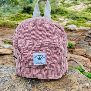 May include: A small, burgundy and white herringbone-patterned backpack with a white handle. The backpack has a small front pocket with a label that reads "Himalayan Hemp THC Free Made in India."