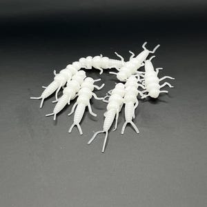 May include: A collection of small, white, insect-like objects with multiple legs and segmented bodies, arranged against a dark background. The objects appear to be made of a smooth, possibly plastic material, and are evenly lit.