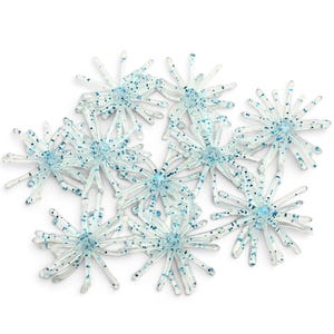 May include: A collection of translucent, star-shaped plastic fishing lures. Each lure features multiple radiating arms with a clear base and embedded blue glitter particles throughout the structure, creating a sparkling, multi-pointed appearance.