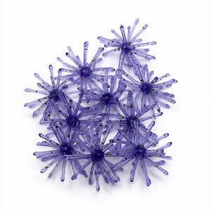 May include: A collection of purple, star-shaped fishing lures made of a translucent, flexible material. Each lure features multiple radiating, thin, tentacle-like arms embedded with small, reflective green glitter particles throughout the structure.
