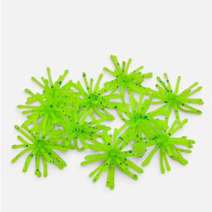 May include: A collection of bright lime green fishing lures, each featuring a central hub with multiple radiating, flexible tentacles. The translucent material is speckled with small, dark blue glitter particles throughout.