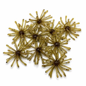 May include: A collection of eight translucent olive-green fishing lures, each shaped like a small sea anemone or spider with multiple radiating, thin, flexible legs. The legs feature small, dark, evenly spaced speckles throughout their length.