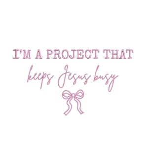 May include: A white background with the pink text "I'M A PROJECT THAT keeps Jesus busy" and a pink bow graphic. The text is in a stylized, embroidered font. The overall design is simple and feminine.