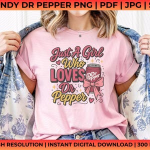 May include: Pink t-shirt with the text "Just A Girl Who Loves Dr Pepper" in a retro design. The graphic includes a Dr Pepper can with a pink bow. The shirt is worn with a denim jacket.