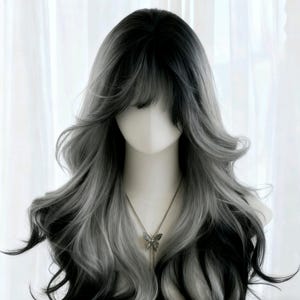 Puede incluir: Una peluca larga y ondulada con un degradado de negro a gris y plateado. La peluca presenta un flequillo completo y está peinada con rizos sueltos. Se ve un collar con colgante de mariposa plateada. La peluca se exhibe en una cabeza de maniquí.