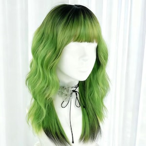 May include: A green and black wig with wavy, shoulder-length hair and a blunt fringe. The wig is displayed on a mannequin head with a gray floral choker. The hair color transitions from black at the roots to a vibrant green.