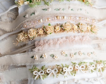 May include: A selection of handcrafted headbands with floral and ribbon detailing. The headbands are made from cream-coloured fabric, decorated with small flowers, pearls, and delicate bows. The colour scheme includes soft pastels and natural tones, creating a vintage aesthetic.