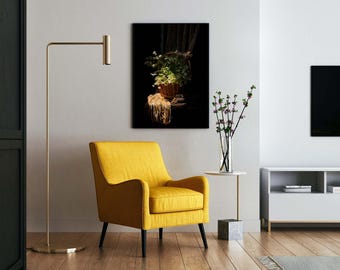 May include: A modern living room scene featuring a yellow armchair with black legs, a gold floor lamp, and a small side table. A framed artwork depicts a still life with a basket of flowers. A vase of flowers sits on the side table.