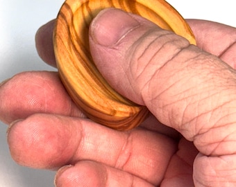 May include: A small, circular wooden object with a smooth, polished finish and a distinct light and dark brown grain pattern. The item features a concave center and a raised, rounded rim, showcasing the natural texture of the wood grain.