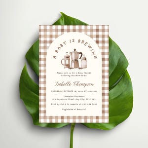 May include: A baby shower invitation with a brown and white gingham border. The invitation features the text "A Baby is Brewing" above illustrations of a coffee pot, a French press, and a baby bottle. The invitation includes the name Isabelle Thompson, date, time, and location.