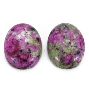 Può includere: Due pietre preziose ovali con un mix di colori. Le pietre hanno una base rosa intenso con macchie verdi e nere. Le pietre preziose sono lucide e lisce, con un aspetto naturale e organico. Le pietre sono su uno sfondo bianco.